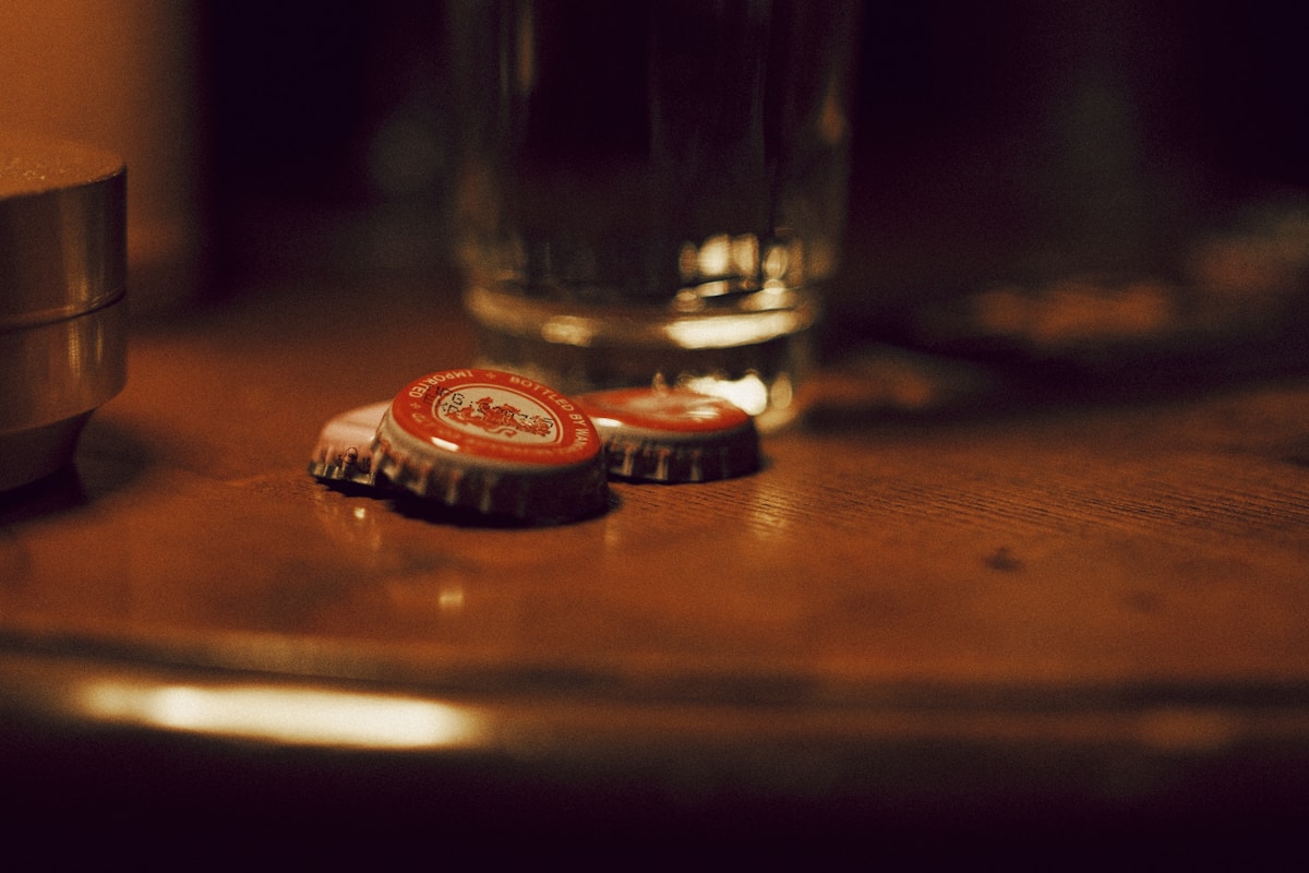 A glass of water set on a table beside red bottle caps.