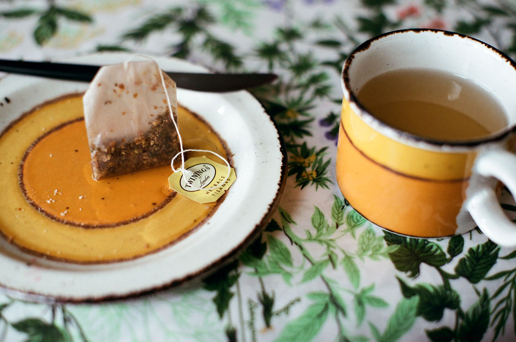 A mug of ginger tea set beside a tea bag on a tabletop.